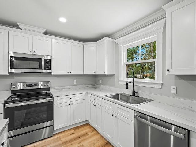 kitchen with sink, white cabinetry, light stone counters, appliances with stainless steel finishes, and light hardwood / wood-style floors