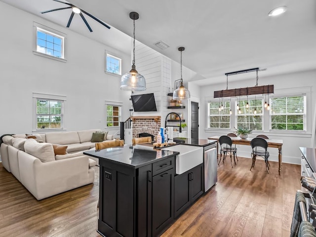 kitchen featuring a center island with sink, a brick fireplace, decorative light fixtures, sink, and stainless steel dishwasher