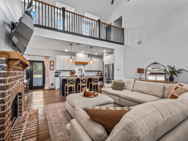 living room featuring a brick fireplace, dark hardwood / wood-style flooring, a high ceiling, and sink