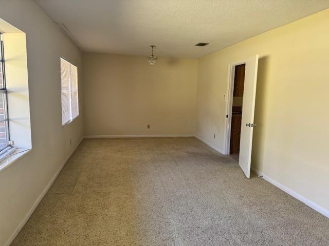 empty room featuring a textured ceiling, light colored carpet, visible vents, and baseboards