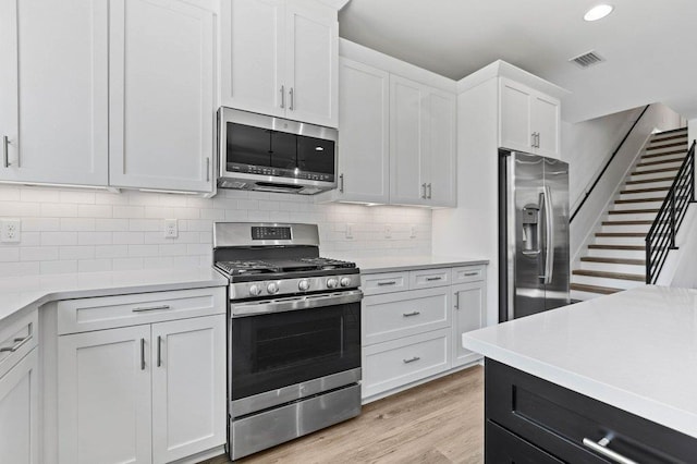 kitchen with light hardwood / wood-style floors, white cabinetry, appliances with stainless steel finishes, and tasteful backsplash