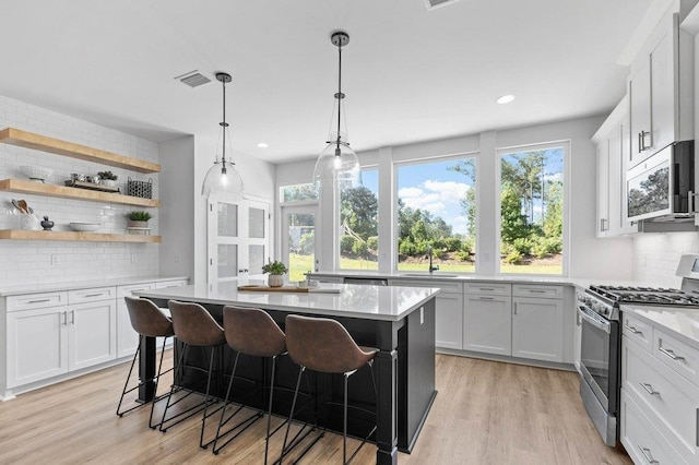 kitchen with tasteful backsplash, stainless steel appliances, white cabinets, a breakfast bar area, and light hardwood / wood-style flooring