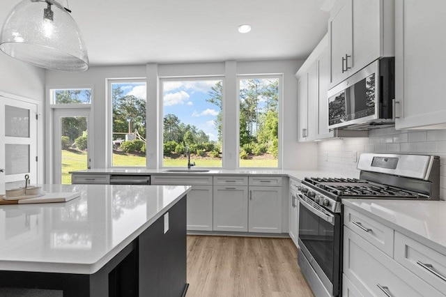 kitchen with white cabinetry, hanging light fixtures, light hardwood / wood-style floors, and stainless steel appliances