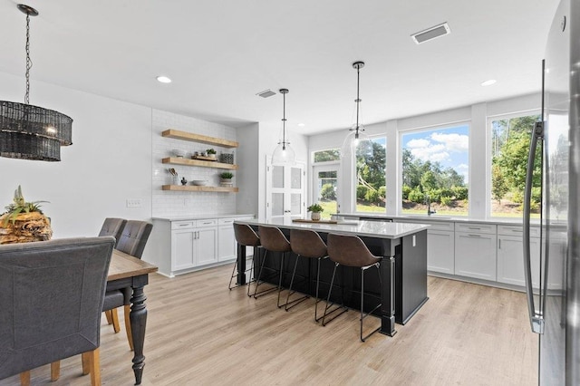 kitchen featuring light hardwood / wood-style floors, white cabinetry, decorative light fixtures, a kitchen island, and decorative backsplash