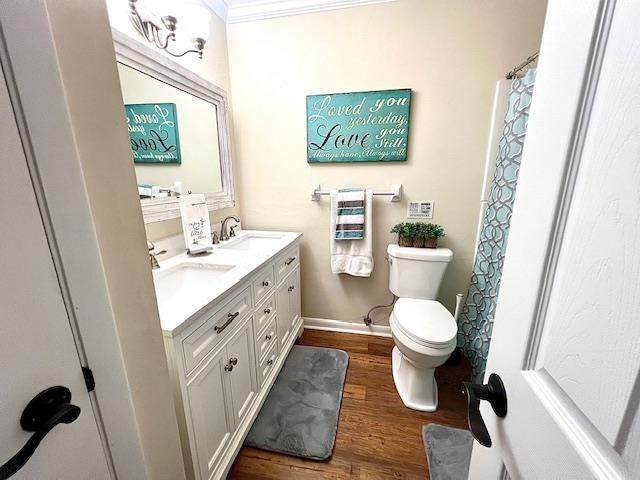 2401 Mexia Ave, Tallahassee, FL 32304 - bathroom featuring wood finished floors, toilet, double vanity, ornamental molding, and baseboards