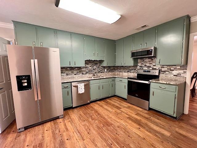 2401 Mexia Ave, Tallahassee, FL 32304 - kitchen featuring appliances with stainless steel finishes, a sink, green cabinets, backsplash, and light wood-style floors