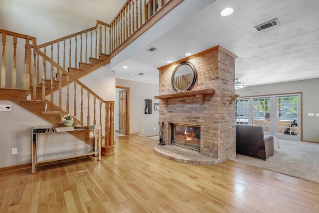 living room featuring visible vents, wood-type flooring, a brick fireplace, and stairway