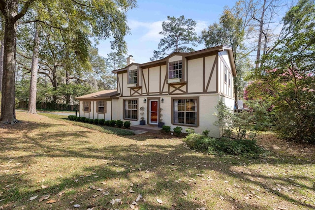 english style home with a front yard, a chimney, and stucco siding