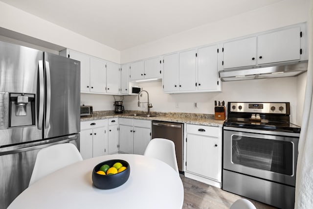 kitchen with under cabinet range hood, stainless steel appliances, wood finished floors, a sink, and white cabinetry