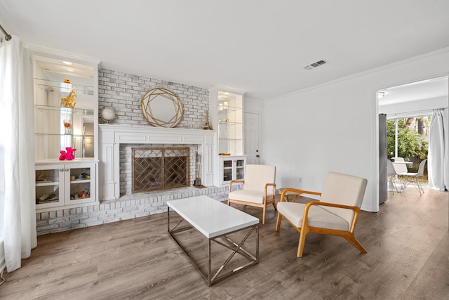 living area with a fireplace, visible vents, wood finished floors, and ornamental molding