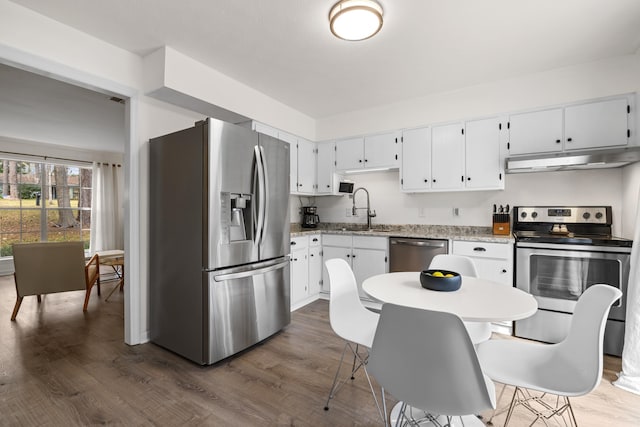 kitchen with dark wood-type flooring, stainless steel appliances, under cabinet range hood, white cabinetry, and a sink