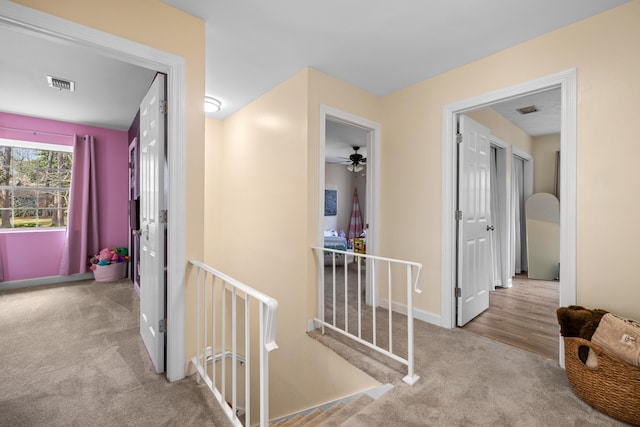 hall with carpet, an upstairs landing, and visible vents