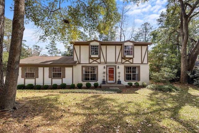 tudor-style house featuring a front lawn and stucco siding