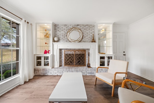 living area with a wealth of natural light, a brick fireplace, crown molding, and wood finished floors