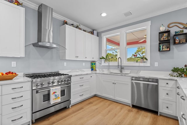 kitchen featuring wall chimney range hood, crown molding, white cabinets, and appliances with stainless steel finishes