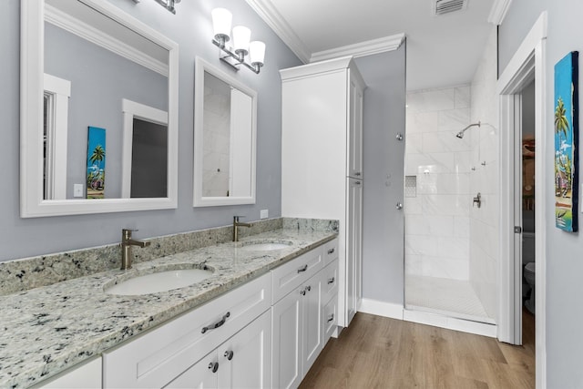 bathroom with hardwood / wood-style floors, a tile shower, vanity, ornamental molding, and toilet