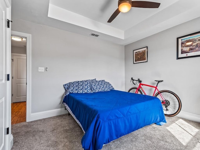 carpeted bedroom with a raised ceiling and ceiling fan