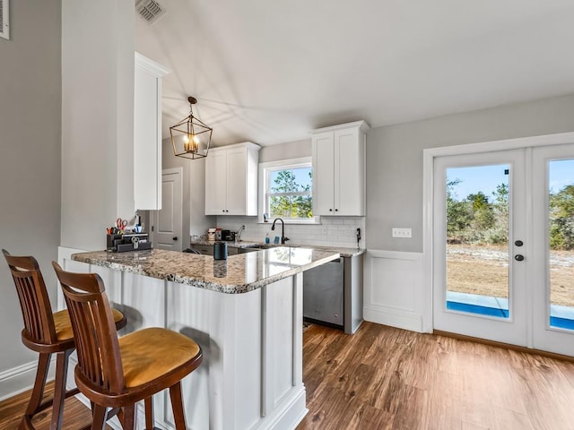 kitchen featuring hardwood / wood-style flooring, white cabinetry, light stone counters, decorative light fixtures, and kitchen peninsula