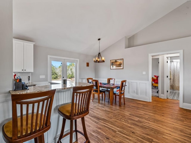 kitchen featuring french doors, lofted ceiling, hanging light fixtures, light stone countertops, and light hardwood / wood-style floors