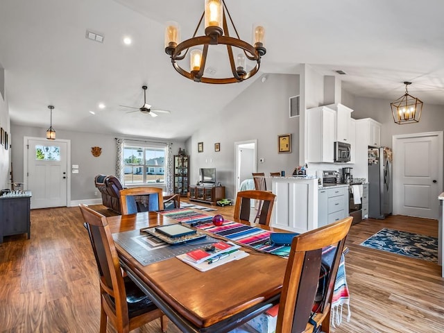 dining space with ceiling fan with notable chandelier, light hardwood / wood-style flooring, and high vaulted ceiling