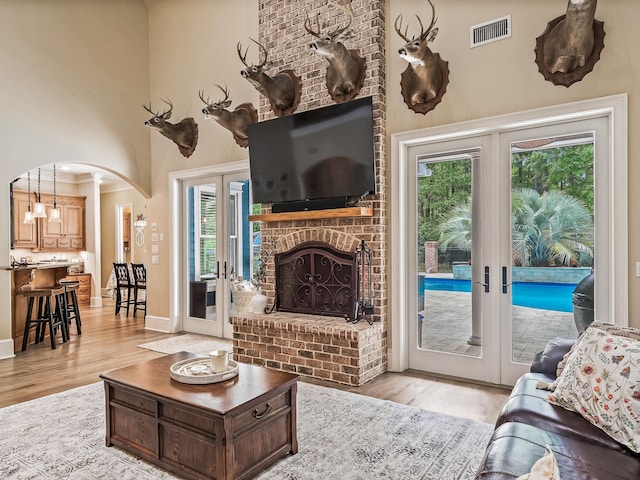 living room with a high ceiling, french doors, a healthy amount of sunlight, and light hardwood / wood-style flooring