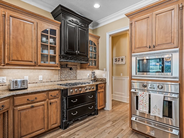 kitchen featuring light wood-type flooring, appliances with stainless steel finishes, crown molding, and light stone countertops