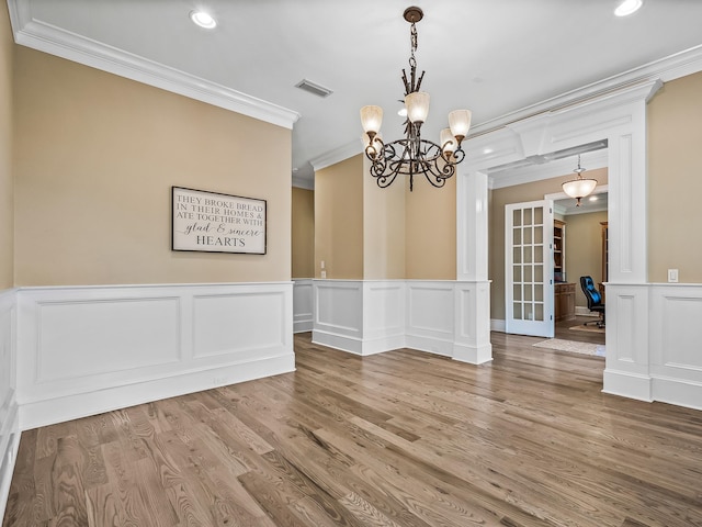 unfurnished dining area with ornamental molding, french doors, hardwood / wood-style flooring, and a chandelier