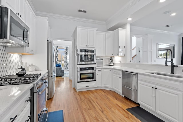 kitchen featuring white cabinetry, stainless steel appliances, ornamental molding, and sink