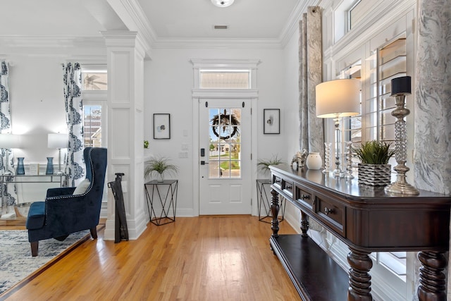 entrance foyer featuring light hardwood / wood-style floors, crown molding, and decorative columns