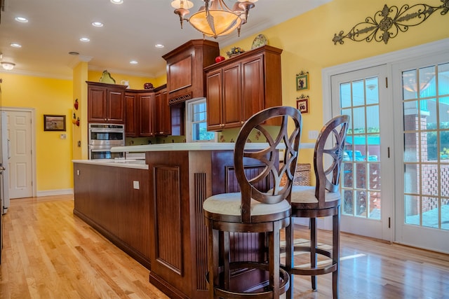 kitchen with a notable chandelier, hanging light fixtures, light hardwood / wood-style flooring, double oven, and crown molding