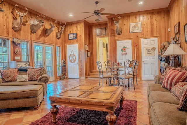 tiled living room with french doors, crown molding, a towering ceiling, wood walls, and ceiling fan