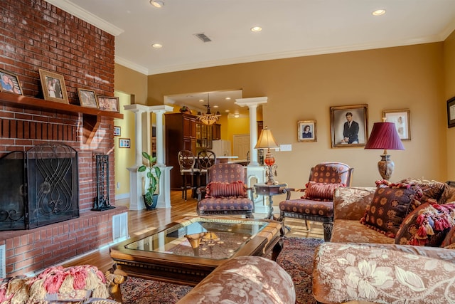 living room featuring decorative columns, hardwood / wood-style flooring, ornamental molding, and a brick fireplace