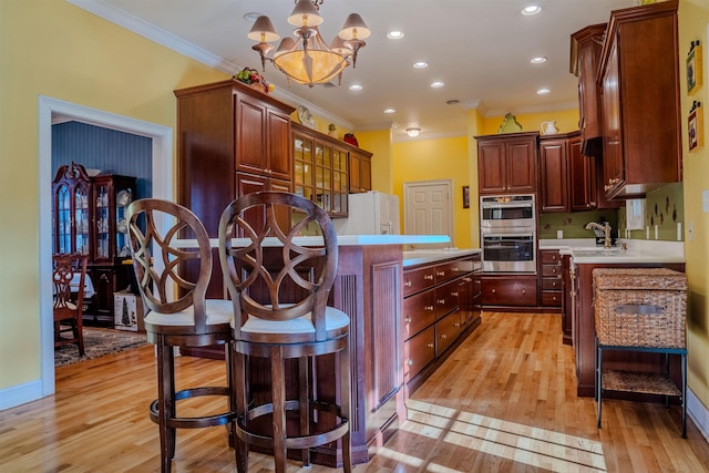 kitchen featuring hanging light fixtures, a chandelier, stainless steel double oven, ornamental molding, and light hardwood / wood-style flooring