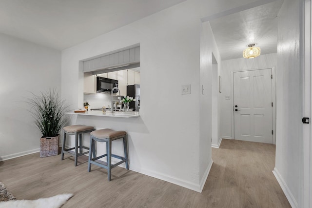 kitchen with light hardwood / wood-style floors, stainless steel refrigerator with ice dispenser, backsplash, a breakfast bar area, and white cabinetry