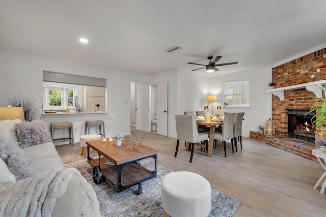 living room with a brick fireplace, ceiling fan, and light hardwood / wood-style floors