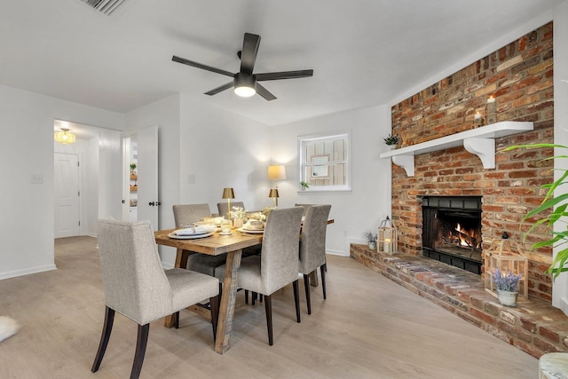 dining area with a fireplace, ceiling fan, and light wood-type flooring