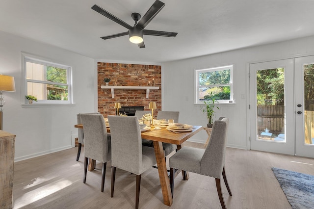 dining space featuring ceiling fan, french doors, light hardwood / wood-style flooring, and a brick fireplace