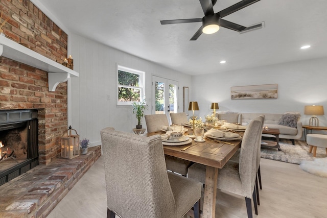 dining space with ceiling fan, light hardwood / wood-style flooring, french doors, and a fireplace