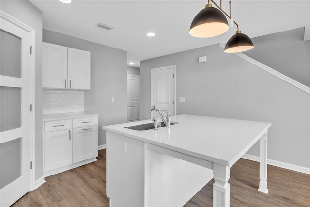 kitchen featuring wood finished floors, a sink, light countertops, white cabinets, and backsplash