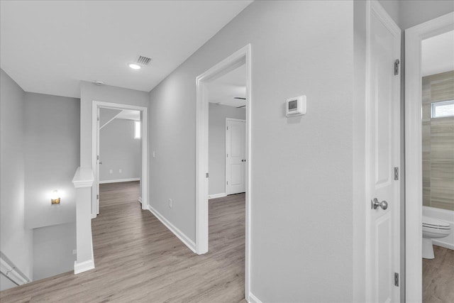 hall featuring visible vents, baseboards, and wood finished floors