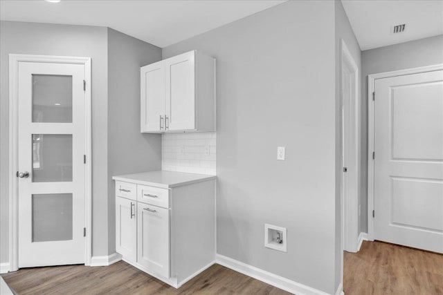 interior space with visible vents, light wood finished floors, light countertops, white cabinets, and backsplash