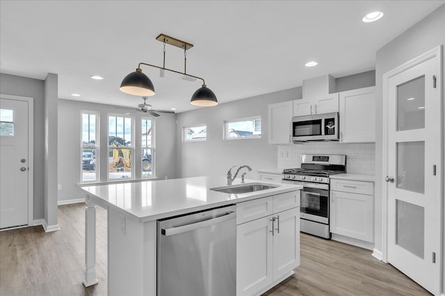 kitchen with a center island with sink, a sink, light countertops, appliances with stainless steel finishes, and backsplash