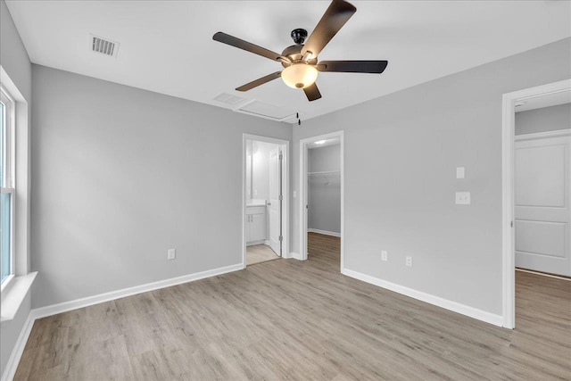 unfurnished bedroom with a spacious closet, wood finished floors, visible vents, and baseboards