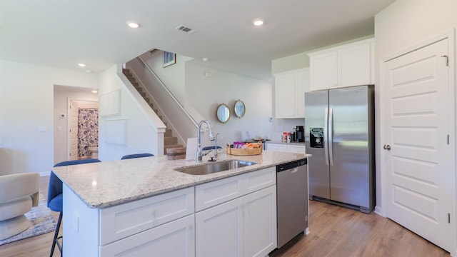 2986 Ervine St, Tallahassee, FL 32308 - kitchen featuring appliances with stainless steel finishes, a center island with sink, white cabinetry, light stone countertops, and light wood-style flooring