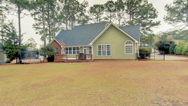 rear view of property featuring a wooden deck, a trampoline, and a lawn