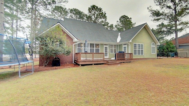 back of property featuring a wooden deck, a yard, and a trampoline