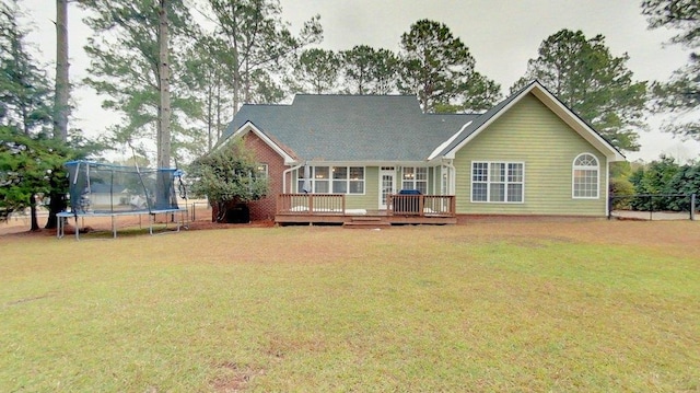 rear view of house with a wooden deck, a yard, and a trampoline