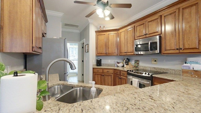 kitchen with sink, ceiling fan, appliances with stainless steel finishes, light stone counters, and ornamental molding