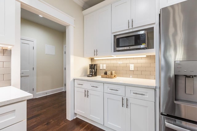 kitchen with white cabinetry, appliances with stainless steel finishes, backsplash, light stone countertops, and dark wood-type flooring