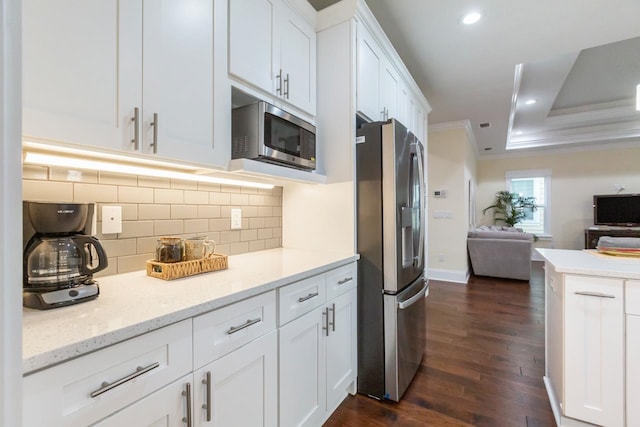 kitchen with appliances with stainless steel finishes, light stone counters, crown molding, white cabinets, and dark wood-type flooring